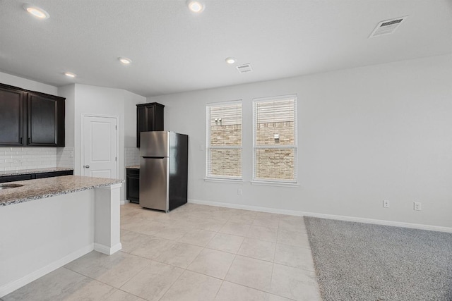 kitchen featuring freestanding refrigerator, tasteful backsplash, light stone countertops, light tile patterned flooring, and recessed lighting