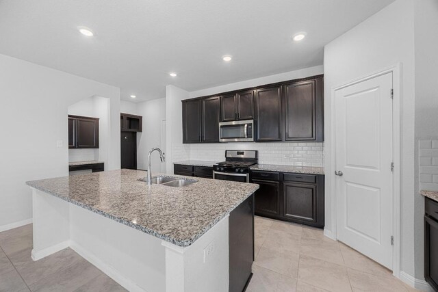 kitchen featuring appliances with stainless steel finishes, a sink, light stone countertops, tasteful backsplash, and a center island with sink
