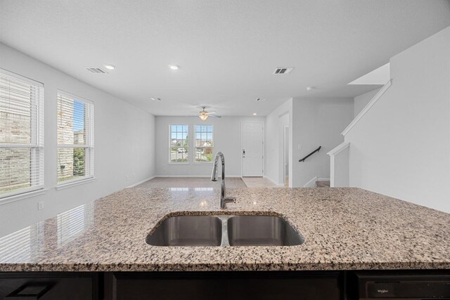 kitchen featuring a sink, ceiling fan, open floor plan, light stone counters, and dishwasher