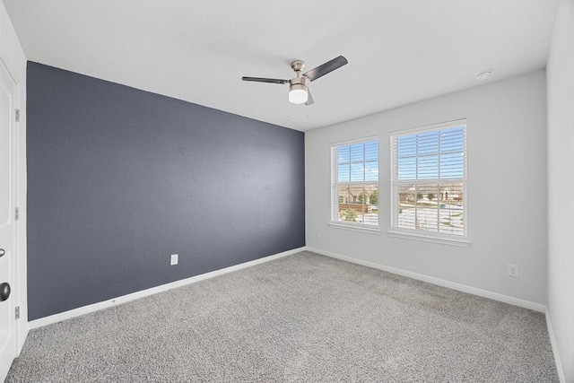carpeted spare room with ceiling fan and baseboards
