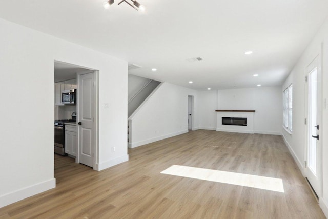 12127 Cabana Ln, Austin, TX 78727 - unfurnished living room featuring light wood-style flooring, a glass covered fireplace, and recessed lighting