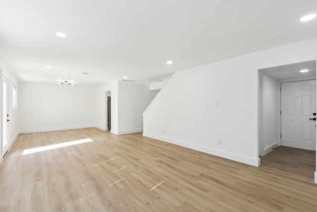 unfurnished living room with recessed lighting, baseboards, light wood finished floors, and stairs