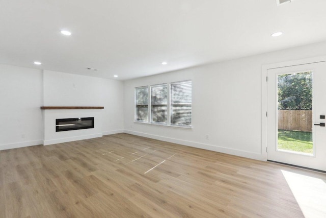 unfurnished living room with light wood-style flooring, a glass covered fireplace, recessed lighting, and baseboards
