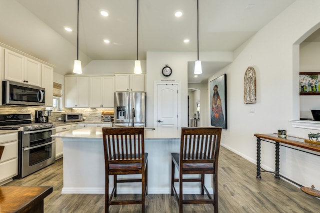 22208 Coyote Cave Trl, Spicewood, TX 78669 - kitchen featuring appliances with stainless steel finishes, a center island, white cabinetry, wood finished floors, and tasteful backsplash