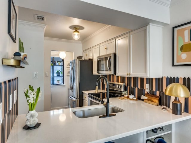 kitchen featuring stainless steel appliances, light countertops, ornamental molding, white cabinets, and a peninsula