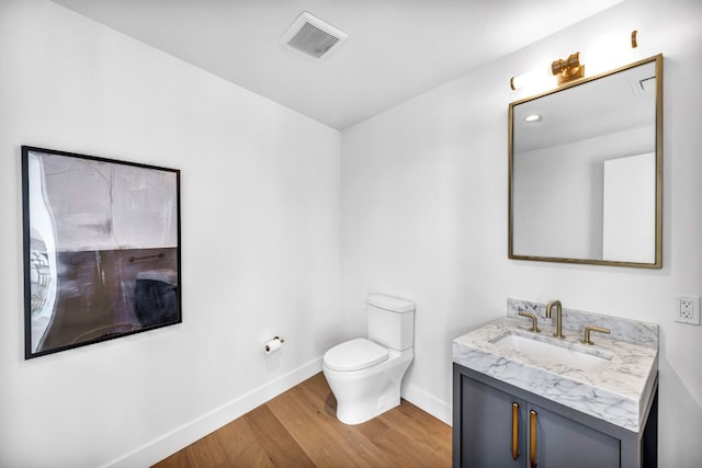 half bathroom featuring wood finished floors, baseboards, toilet, and vanity