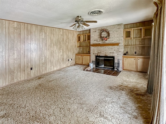 419 N Knox Ave, Giddings, TX 78942 - unfurnished living room featuring ceiling fan, wood walls, a brick fireplace, carpet flooring, and a textured ceiling