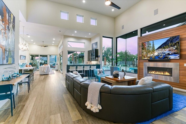 living area featuring a high ceiling, wood finished floors, a glass covered fireplace, plenty of natural light, and recessed lighting