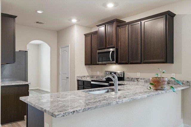 321 Freedom Park Ave, Liberty Hill, TX 78642 - kitchen with appliances with stainless steel finishes, a sink, dark brown cabinets, arched walkways, and a peninsula