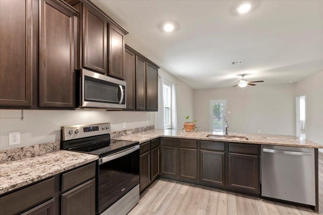 321 Freedom Park Ave, Liberty Hill, TX 78642 - kitchen with stainless steel appliances, a sink, dark brown cabinetry, a peninsula, and light wood-type flooring