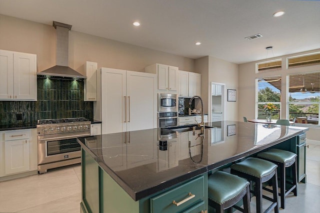 kitchen with appliances with stainless steel finishes, wall chimney range hood, a sink, backsplash, and a kitchen island with sink