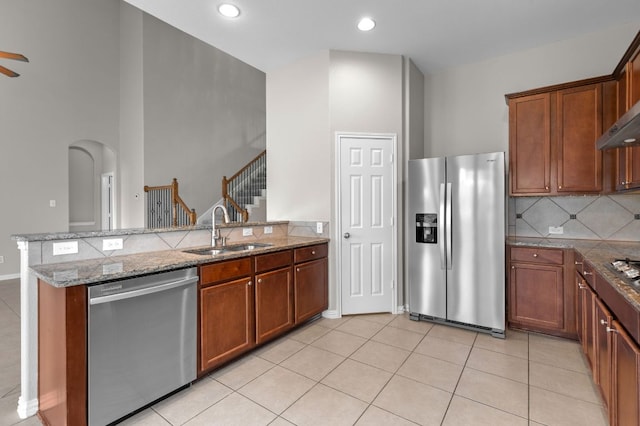 2640 Estefania Ln, Round Rock, TX 78665 - kitchen with appliances with stainless steel finishes, a peninsula, light stone counters, brown cabinets, and a high ceiling