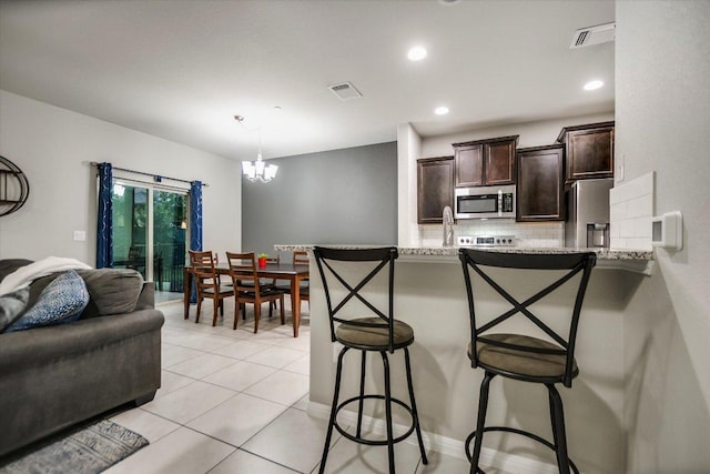 516 E Slaughter Ln Unit 1203, Austin, TX 78744 - kitchen with stainless steel appliances, dark brown cabinetry, a kitchen breakfast bar, tasteful backsplash, and recessed lighting