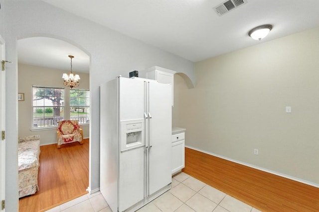 9403 Brandts Wood St, Austin, TX 78744 - kitchen featuring white fridge with ice dispenser, arched walkways, white cabinetry, a chandelier, and light tile patterned floors