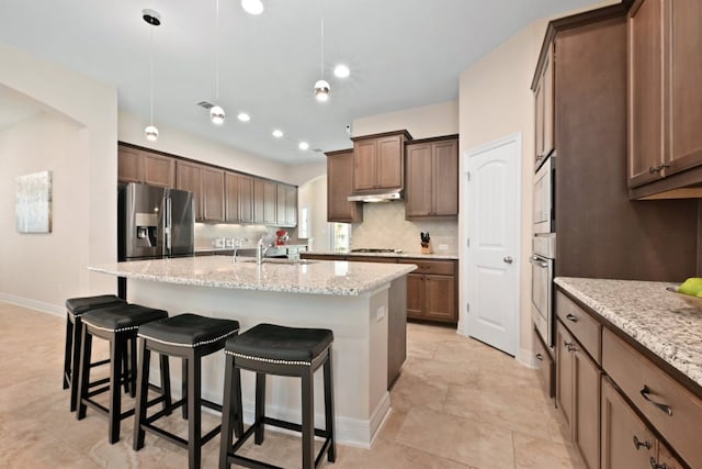6321 Llano Stage Trl, Austin, TX 78738 - kitchen with stainless steel appliances, a breakfast bar area, a sink, under cabinet range hood, and a center island with sink