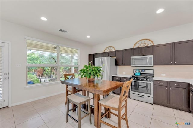kitchen with stainless steel appliances, dark brown cabinets, light countertops, light tile patterned floors, and baseboards