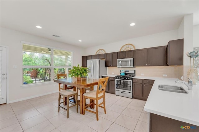 kitchen with appliances with stainless steel finishes, a sink, light countertops, backsplash, and dark brown cabinets