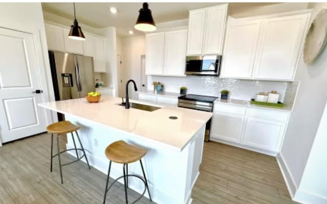 2585 Jack Nora Way, Round Rock, TX 78665 - kitchen featuring stainless steel appliances, a sink, white cabinets, light wood-type flooring, and a breakfast bar area