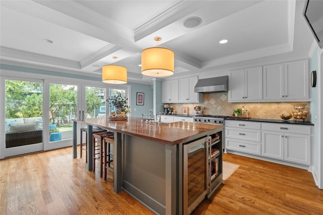 1704 W 34th St, Austin, TX 78703 - kitchen featuring wine cooler, wall chimney exhaust hood, tasteful backsplash, white cabinetry, and light wood finished floors