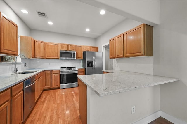 1502 Medio Calle, Austin, TX 78733 - kitchen with appliances with stainless steel finishes, light wood-style flooring, a peninsula, tasteful backsplash, and light stone countertops