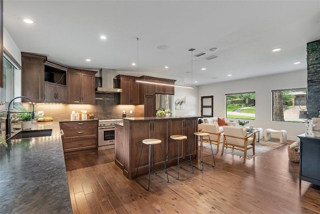 2502 Spring Creek Dr, Austin, TX 78704 - kitchen with a sink, wall chimney range hood, appliances with stainless steel finishes, a kitchen island, and a kitchen bar