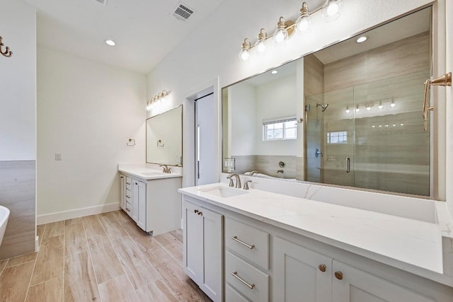 2803 Wilson Ave, Lago Vista, TX 78645 - full bathroom featuring two vanities, a freestanding tub, a shower stall, wood finished floors, and recessed lighting