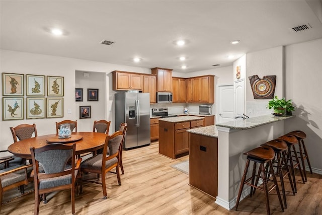 805 Willow Creek Cir, San Marcos, TX 78666 - kitchen with appliances with stainless steel finishes, light wood finished floors, a peninsula, a center island, and recessed lighting