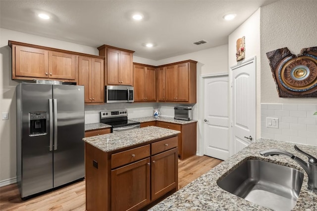 805 Willow Creek Cir, San Marcos, TX 78666 - kitchen featuring appliances with stainless steel finishes, a sink, light stone counters, light wood-type flooring, and backsplash