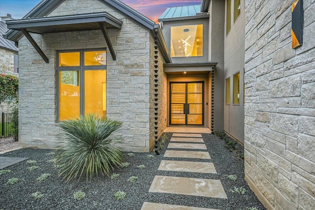 98 Wennmohs Pl, Horseshoe Bay, TX 78657 - exterior entry at dusk with stone siding, a standing seam roof, metal roof, and fence
