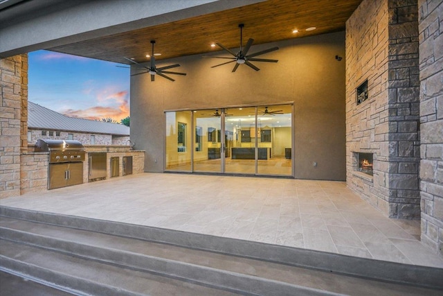 98 Wennmohs Pl, Horseshoe Bay, TX 78657 - patio terrace at dusk with exterior kitchen, a grill, a ceiling fan, and an outdoor stone fireplace