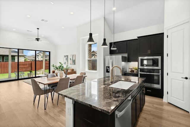 300 Barrel Bnd, Georgetown, TX 78628 - kitchen featuring appliances with stainless steel finishes, dark cabinetry, ceiling fan, a center island with sink, and light wood finished floors