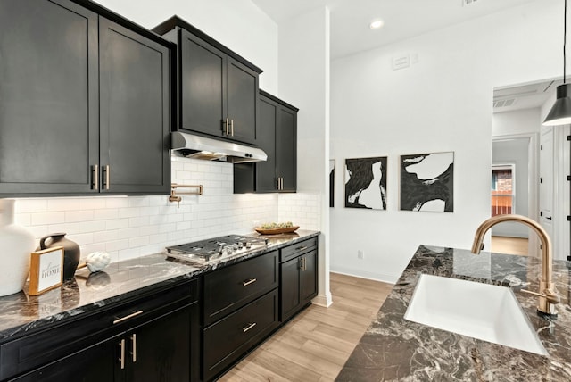 300 Barrel Bnd, Georgetown, TX 78628 - kitchen with under cabinet range hood, stainless steel gas stovetop, dark cabinets, and dark stone counters