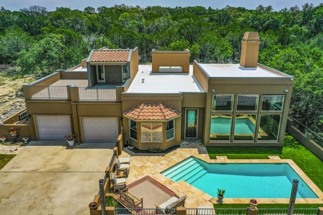 3211 Constitution Dr, Lago Vista, TX 78645 - rear view of house featuring stucco siding, a chimney, concrete driveway, and a wooded view
