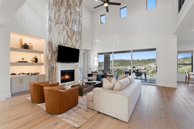 6901 Davenport Divide Rd, Austin, TX 78738 - living room with a high ceiling, a warm lit fireplace, light wood-style floors, ceiling fan, and baseboards