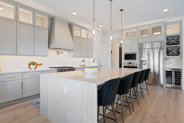 6901 Davenport Divide Rd, Austin, TX 78738 - kitchen featuring built in appliances, custom range hood, wine cooler, light wood-style floors, and an island with sink