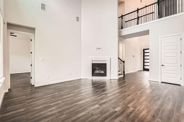 461 Constitution Way, Kyle, TX 78640 - unfurnished living room with a towering ceiling, dark wood-style floors, baseboards, a glass covered fireplace, and stairway