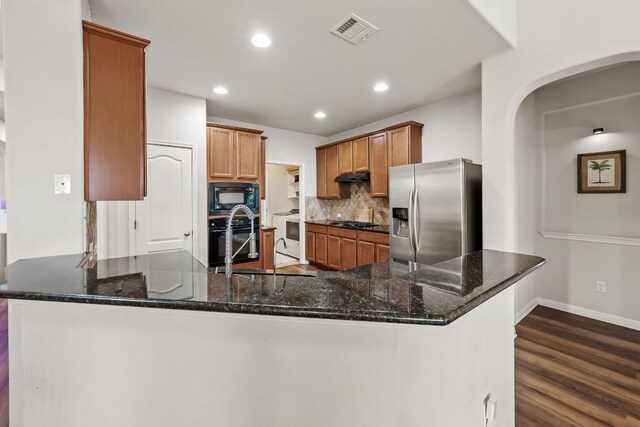 4404 Cierne Cv, Round Rock, TX 78681 - kitchen with black appliances, a peninsula, dark wood finished floors, decorative backsplash, and dark stone countertops