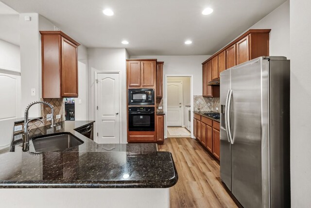 4404 Cierne Cv, Round Rock, TX 78681 - kitchen featuring black appliances, a sink, a peninsula, light wood-style flooring, and tasteful backsplash