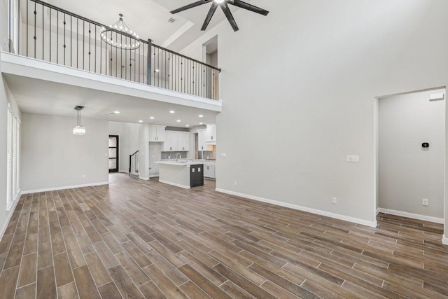 125 Bauer Loop, Liberty Hill, TX 78642 - unfurnished living room with a towering ceiling, a ceiling fan, a chandelier, dark wood-style flooring, and recessed lighting