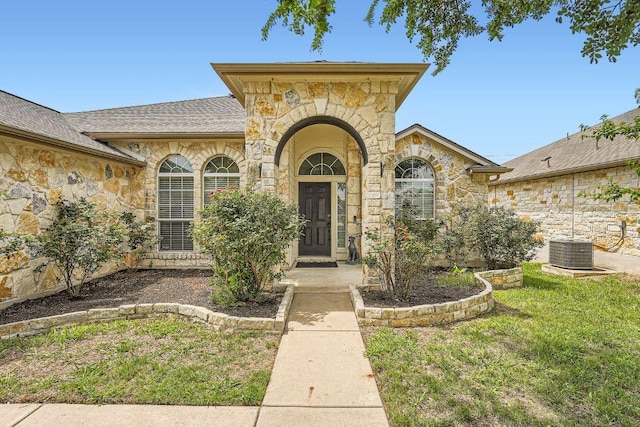 134 Sassafras St, Hutto, TX 78634 - entrance to property with stone siding, central AC unit, roof with shingles, and a lawn