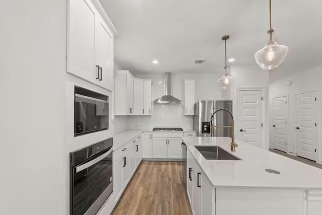16917 Santiaguillo Trce, Manor, TX 78653 - kitchen with appliances with stainless steel finishes, wall chimney exhaust hood, a sink, light countertops, and a kitchen island with sink