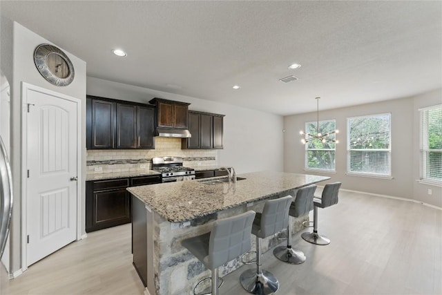6739 Indian Lndg, San Antonio, TX 78253 - kitchen with stainless steel gas stove, light wood-style floors, light stone countertops, decorative backsplash, and a kitchen breakfast bar