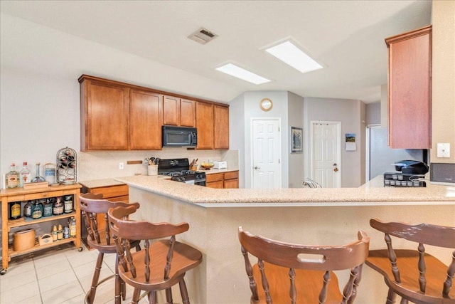 15115 Staked Plains Loop, Austin, TX 78717 - kitchen with gas range oven, black microwave, brown cabinetry, and a kitchen breakfast bar
