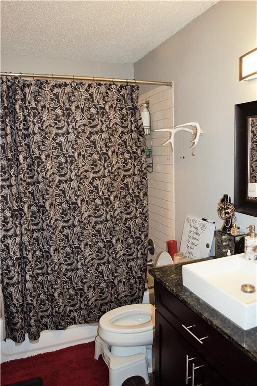 1320 Southport Dr, Austin, TX 78704 - full bath with vanity, toilet, shower / tub combo with curtain, and a textured ceiling