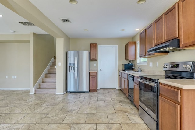 8912 Norwich Castle, Austin, TX 78747 - kitchen featuring appliances with stainless steel finishes, under cabinet range hood, light countertops, brown cabinets, and light stone finish floors