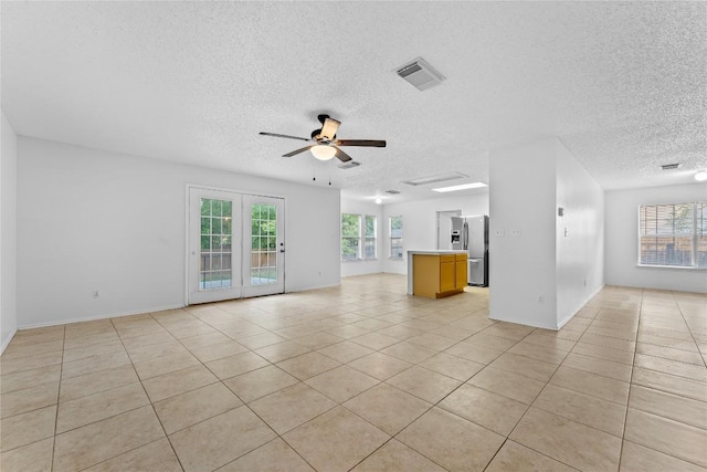 491 Emerald Fields Ln, Kyle, TX 78640 - unfurnished living room featuring a textured ceiling, healthy amount of natural light, a ceiling fan, light tile patterned floors, and baseboards