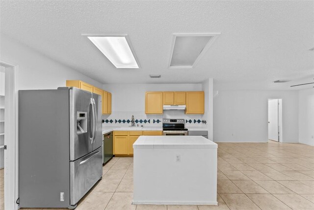 491 Emerald Fields Ln, Kyle, TX 78640 - kitchen with appliances with stainless steel finishes, under cabinet range hood, light brown cabinets, a kitchen island, and light tile patterned floors