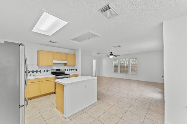 491 Emerald Fields Ln, Kyle, TX 78640 - kitchen with appliances with stainless steel finishes, under cabinet range hood, a kitchen island, light tile patterned floors, and light brown cabinetry
