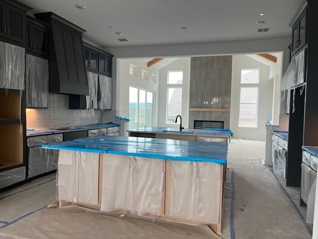 19217 Hopper Ln, Austin, TX 78738 - kitchen with a tile fireplace, decorative backsplash, a kitchen island, extractor fan, and dark cabinetry