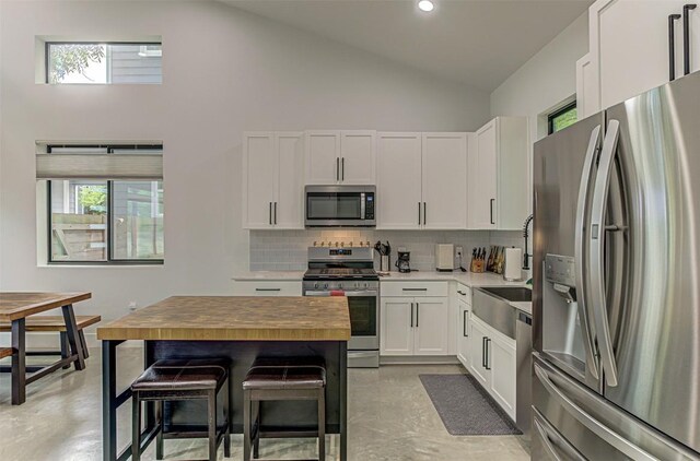 600 Blackson Ave Unit 2, Austin, TX 78752 - kitchen with stainless steel appliances, backsplash, high vaulted ceiling, white cabinetry, and concrete flooring